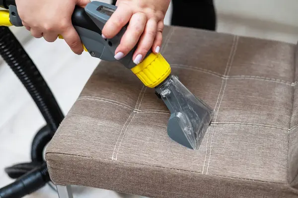 Kadın, elektrikli süpürgeyle kumaş sandalyesini temizliyor.