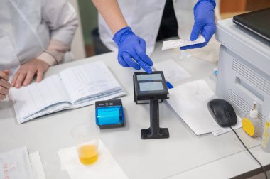 A narcologist tests urine for drugs using an electronic device clipart