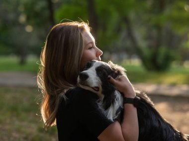 Beyaz bir kadın parkta yürürken köpeğine sarılıyor.