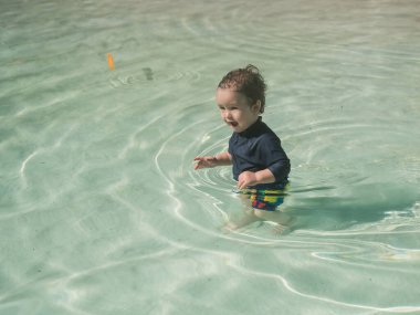 Bir yaşında beyaz bir çocuk kumlu poposu olan bir havuzda yüzüyor.