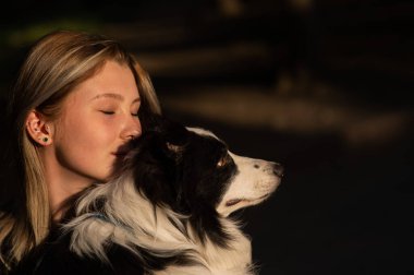 Beyaz bir kadın parkta yürürken köpeğine sarılıyor.