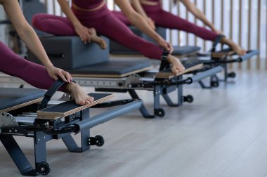 Pembe spor kıyafetli üç Asyalı kadın ıslah yatağıyla pilates egzersizi yapıyor.