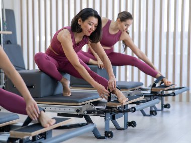 Pembe spor kıyafetli üç Asyalı kadın ıslah yatağıyla pilates egzersizi yapıyor.