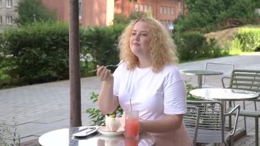 Caddedeki kafede kek yiyen şişman beyaz kadın.