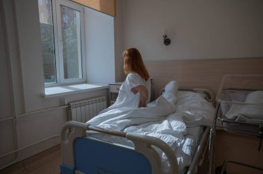 Mutsuz bir kadın kanepeye oturur ve doğum yaptıktan sonra karnını bir hastane odasında tutar.