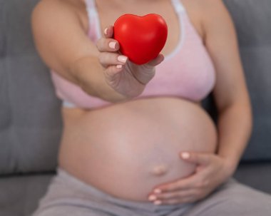 Beyaz, hamile, karnı üzerinde kalbi olan bir kadın. Üçüncü üç aylık dönem