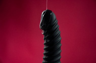 Lube pouring on black dildo on pink background