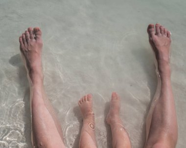 Deniz kıyısındaki bir çocuğun ve annesinin bacaklarının en üst görüntüsü.