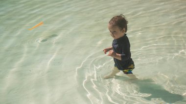 Bir yaşında beyaz bir çocuk kumlu poposu olan bir havuzda yüzüyor.