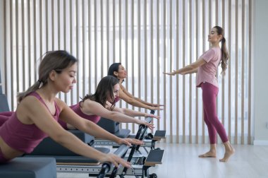 Pembe spor kıyafetli üç kadın ıslah yatağıyla pilates egzersizi yapıyor.