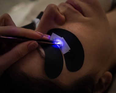 Kirpik uzatma prosedüründen geçen bir kadın ultraviyole lamba kullanıyor.