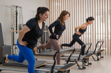 Üç Asyalı kadın bir reformcu üzerinde pilates yapıyor.