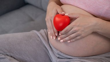 Beyaz, hamile, karnı üzerinde kalbi olan bir kadın. Üçüncü üç aylık dönem