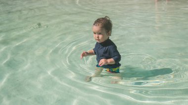Bir yaşında beyaz bir çocuk kumlu poposu olan bir havuzda yüzüyor.