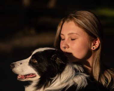 Beyaz bir kadın parkta yürürken köpeğine sarılıyor.