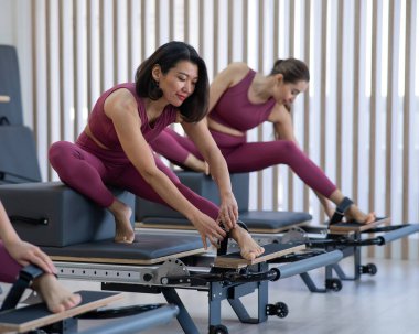 Pembe spor kıyafetli üç Asyalı kadın ıslah yatağıyla pilates egzersizi yapıyor.