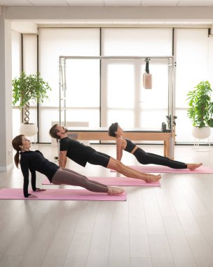 İki kadın ve bir erkek stüdyoda yoga yapıyorlar.