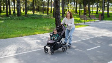 Beyaz kadın bebek arabasıyla küçük oğluyla paten kayıyor.