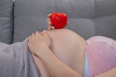 Beyaz, hamile, karnı üzerinde kalbi olan bir kadın. Üçüncü üç aylık dönem