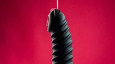 Lube pouring on black dildo on pink background