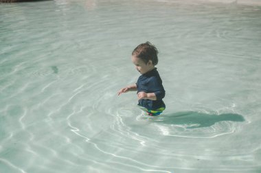 Bir yaşında beyaz bir çocuk kumlu poposu olan bir havuzda yüzüyor.