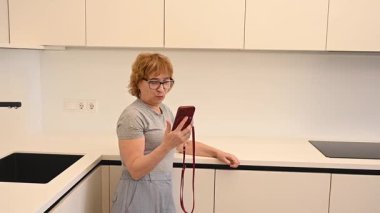 Kafkasyalı yaşlı bir kadın mutfaktaki akıllı telefonuyla video görüşmesi yapıyor.