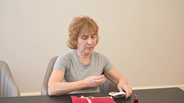 Yaşlı beyaz bir kadın ruj sürüyor ve küçük bir aynaya bakıyor.