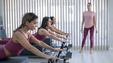 Pembe spor kıyafetli üç kadın ıslah yatağıyla pilates egzersizi yapıyor.