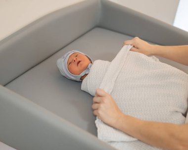 Genç anne yeni doğmuş bebeği masa değişiminde kundaklıyor.