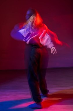 Genç bir kadın mavi ve kırmızı ışıkta çağdaş dans ediyor. Uzun pozlama. Dikey fotoğraf