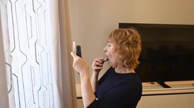 Yaşlı beyaz bir kadın ruj sürüyor.