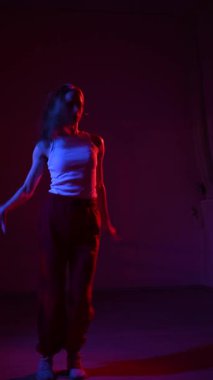Genç bir kadın mavi ve kırmızı ışıkta çağdaş dans ediyor. Dikey video