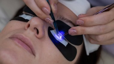 Kirpik uzatma prosedüründen geçen bir kadın ultraviyole lamba kullanıyor.