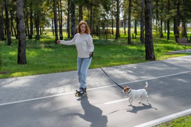 Beyaz kadın, Jack Russell Terrier köpeğiyle parkta paten kayıyor.