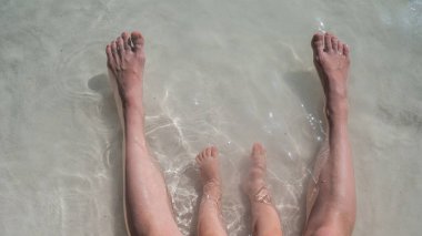 Deniz kıyısındaki bir çocuğun ve annesinin bacaklarının en üst görüntüsü.