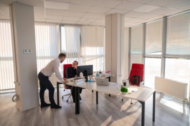 Beyaz adam çalışma masasında durmuş iş hakkında konuşuyor.