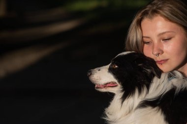 Beyaz bir kadın parkta yürürken köpeğine sarılıyor.