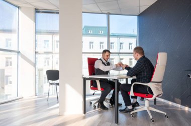 İki beyaz adam bir iş toplantısında birbirlerini selamlıyorlar.