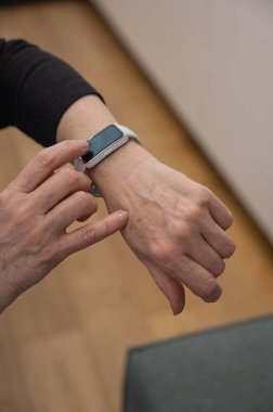 Kafkasyalı yaşlı bir kadın akıllı saate bakıyor. Ellerin yakın çekimi