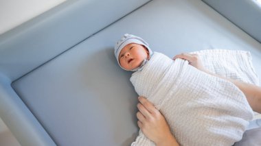 Kadın yeni doğmuş bebeği masa değişiminde kundaklıyor.