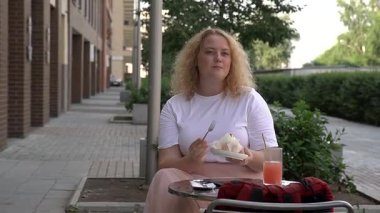 Caddedeki kafede kek yiyen şişman beyaz kadın.