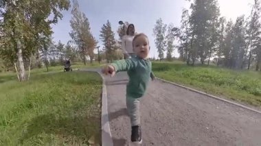 Komik çocuk annesiyle yürürken kamerayı yakalamaya çalışıyor ve kollarını açıyor.
