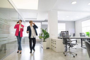 İki meslektaş ofiste yürüyor ve telefonda konuşuyorlar.