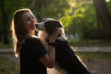 Beyaz bir kadın parkta yürürken köpeğine sarılıyor.