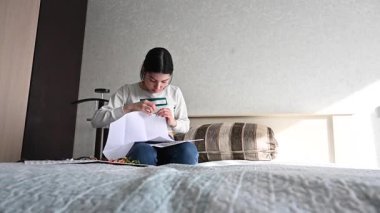 Genç beyaz kadın yatakta otururken çapraz dikiş atıyor.