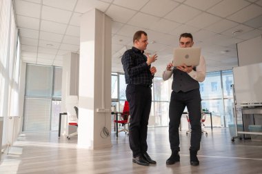 İki beyaz adam dizüstü bilgisayara bakıyor ve iş tartışıyorlar.