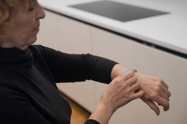 Kafkasyalı yaşlı bir kadın akıllı saate bakıyor. Ellerin yakın çekimi