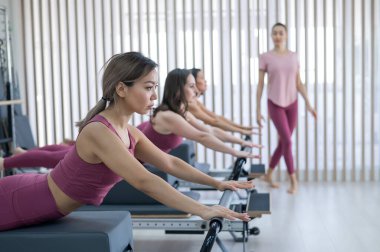 Pembe spor kıyafetli üç kadın ıslah yatağıyla pilates egzersizi yapıyor.