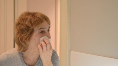 Yaşlı beyaz bir kadın makyajını mendille temizliyor.