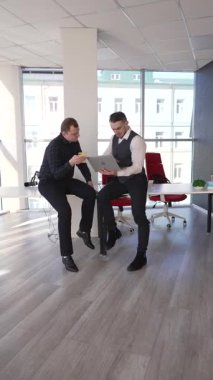 İki beyaz adam dizüstü bilgisayara bakıyor ve iş tartışıyorlar.